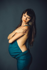 Fototapeta premium delicate and sensual pregnant woman in blue denim overalls on a dark background, under the overalls without clothes