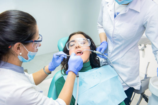 Dentists working with patient. Lady in safety glasses. Qualified dental specialists.