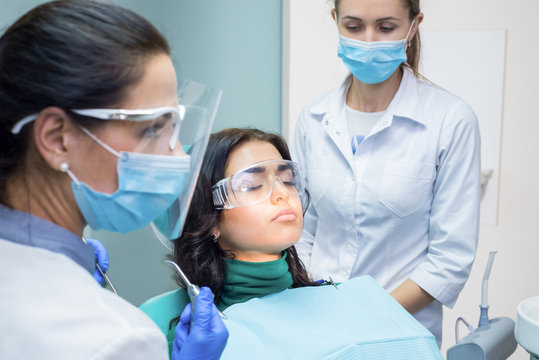 Dentists working at the office. Patient wearing dental safety glasses.