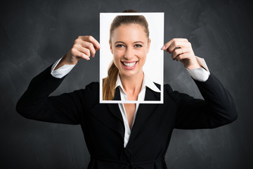 junge Geschäftsfrau hält Schild mit lächelndem Portrait vor ihr Gesicht