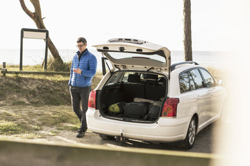 Full length of man using smart phone while walking by car on road