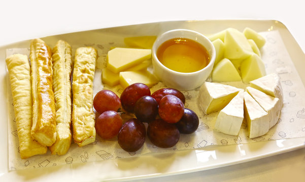 cheese plate with honey saucer grapes and bread stick close up photo