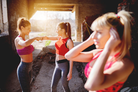 After workout girls clapping hands smiling positive energy. Group fitness people celebrating success at abandoned factory, hot summer day sunshine.