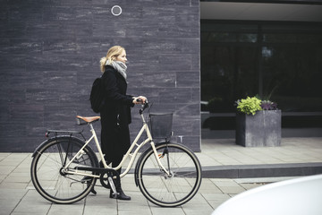 Full length side view of mid adult woman with bicycle walking by building