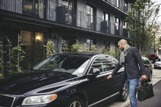 Mid adult businessman holding briefcase while opening car door