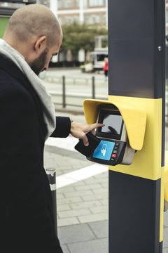 Side view of businessman operating ticket scanner on sidewalk in city