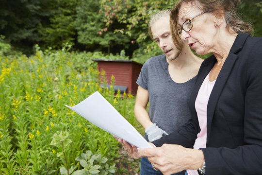 Senior garden architect analyzing blueprint with colleague at yard