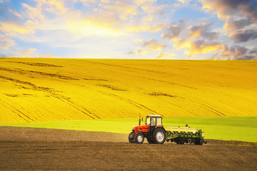Obraz premium Tractor agrimotorworking the ground. Different parts of the field, green yellow, black. Beautiful sky, hilly terrain. Season of agricultural works. 