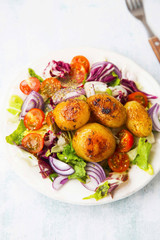 Spiced baked new potatoes in a plate with vegetables salad with onion, green lettuce, tomatoes