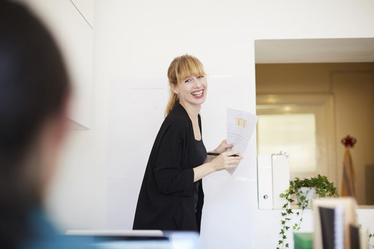 Smiling mid adult businesswoman holding document while looking at colleague in office