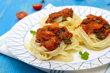 Pasta nest tagliatelle with bolognese sauce and vegetables on a plate.