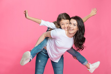 Happy mother piggybacking adorable little daughter smiling at camera