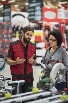 Salesman explaining power tools to mature woman in hardware store