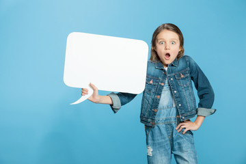 Shocked little girl holding blank speech bubble on blue