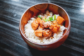 Asian cuisine - rice in sauce with stir fried vegetables and salmon in wooden bowl. Close up.