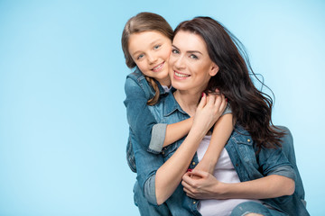 portrait of happy mother and daughter hugging in studio on blue