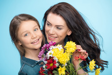 happy mother and daughter hugging and holding flowers in studio on blue, Happy mothers day