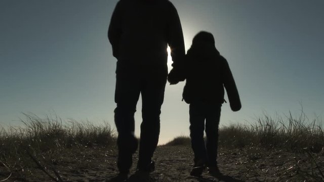 A dad and his little boy walk on beach and up sand dune on bright and beautiful sunny day.