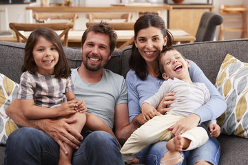 Portrait Of Smiling Family Sitting On Sofa At Home