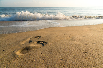 Footprint in sand on the beach with wave and beatiful sunrise sky.