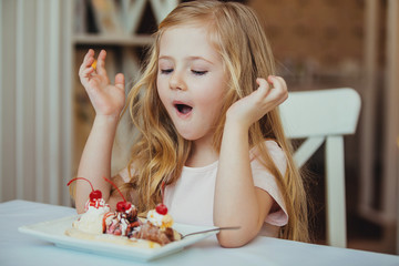 Happy surprised little girl serving ice cream sundae in your coffee .The child sits at a table in a...