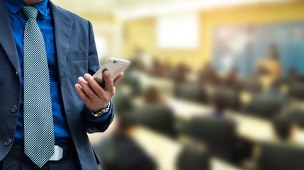 businessman using the mobile phone, blurred of conference hall or seminar room with attendee background.