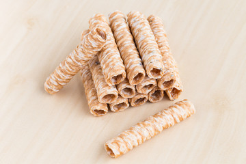 Crispy rolled wafer sticks, traditional dessert in Thailand, are collocated on the wood board.