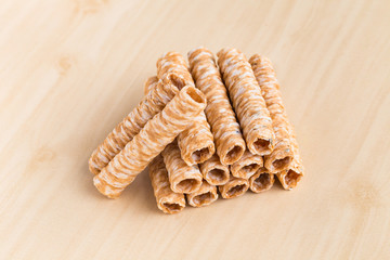 Crispy rolled wafer sticks, traditional dessert in Thailand, are collocated on the wood board.