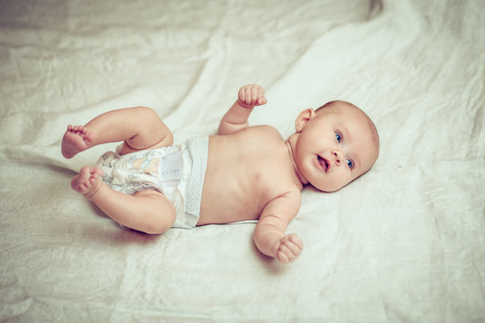 happy baby lying on white sheet and holding his legs