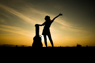 silhuette of woman with guitar case on sunset background