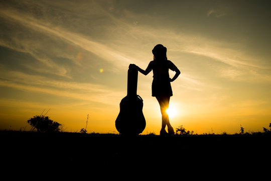 Silhuette Of Woman With Guitar Case On Sunset Background