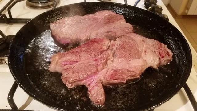 Two fat juicy steaks from marbled beef are fried in oil in a frying pan