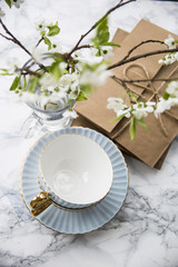 Letters in craft envelopes with a bow on a marble table next to tea cups and a vase with spring flowering branches