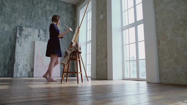 Barefoot female artist painting on a sunlight in her bautiful studio