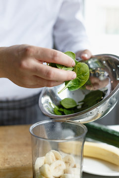 Faceless shot of male chef putting spinach leaved in content while preparing moothie.