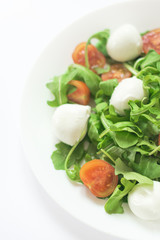 Salad with rocket salad, fresh mozzarella and cherry tomatoes on a white plate and a white background. Top viev