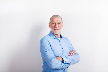 Senior man in light blue shirt smiling, studio shot.