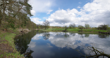 Calm river bend with reflection of cloudy sky. Skyline of Poland.