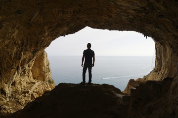 Hiker pauses to watch the sea from a cave, Grotta dei Falsari,  Noli, Liguria, Italy
