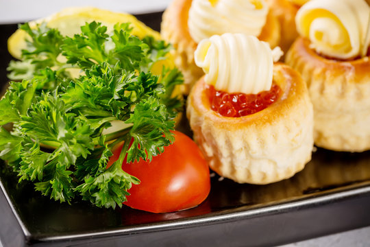 Caviar tarlets with butter. Herbs and tomato on foreground. Close up with selective focus