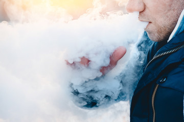 man is vape steam smoking an e-cigarette on the sunset.