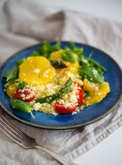 Couscous salad With orange, spinach leaves, asparagus, cherry tomatoes and basil in a blue rustic dish with copy space. Vegetarian food Concept 