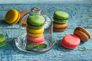 Green, pink and yellow french macarons under the glass on the wooden boards