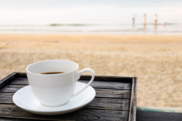 Close up white coffee cup on wood table at sunrise sand beach in the morning