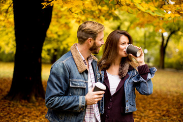 Happy young couple with coffee cups walking in autumn park
