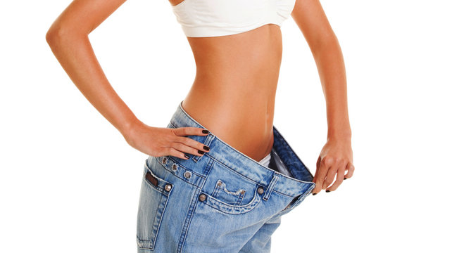 Woman shows her weight loss by wearing an old jeans, isolated on white background. Close up of sporty and beautiful female body.  Healthy lifestyle, dieting, fitness, weight loss concept