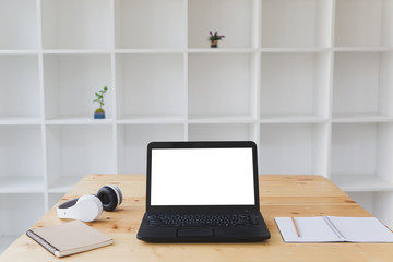 Desk table with laptop, headphone, notepad with white bookshelf background