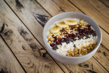 Oatmeal with bananas, cranberry, chia seeds, coconut shreds, almonds. Healthy breakfast concept. Rustic wooden background.