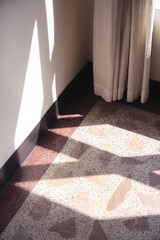 Early morning light streaming through a window and onto a floor made of terrazzo tiles and wall.