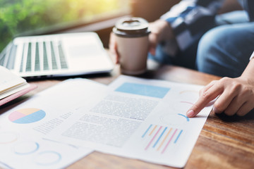 Business woman hands holding cup of coffee. Graph financial  diagram documents with laptop on wooden table at the office.